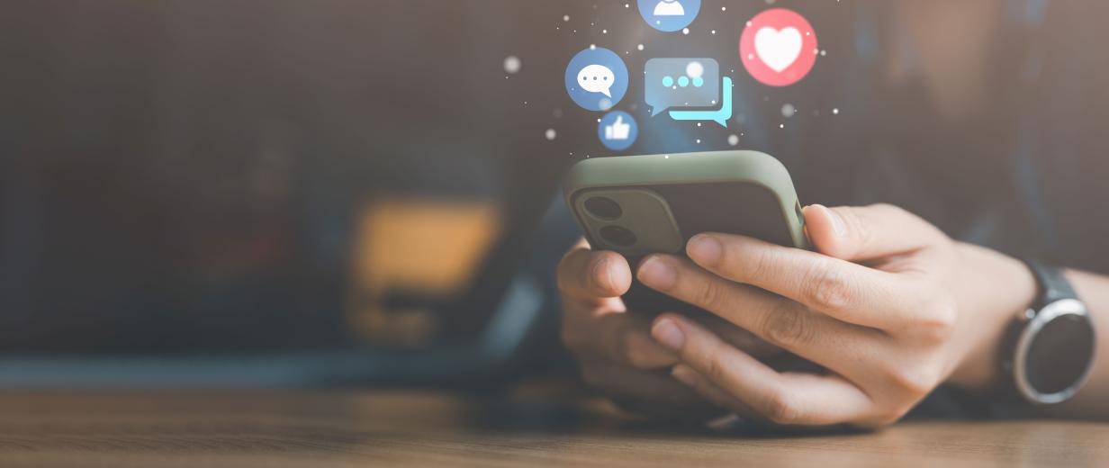 Smartphone Schulung Eltern Qualivit Soziale Medien Zwei Hände halten ein Smartphone, über dem Icons aus Sozialen Medien schweben.