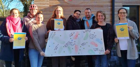 Eine Personengruppe mit Plakaten in den Händen steht vor einem Haus mit Holzfassade.