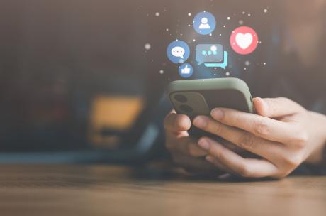 Zwei Hände halten ein Smartphone, über dem Icons aus Sozialen Medien schweben.