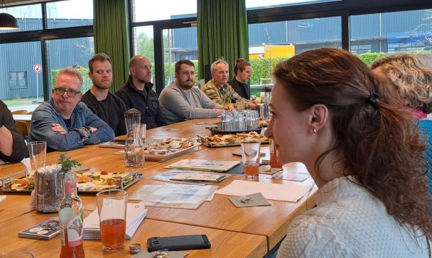 Eine Personengruppe sitzt um einen großen Tisch herum.
