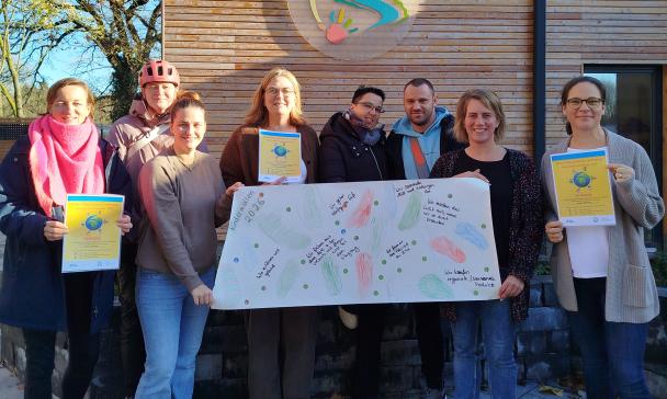 Eine Personengruppe mit Plakaten in den Händen steht vor einem Haus mit Holzfassade.